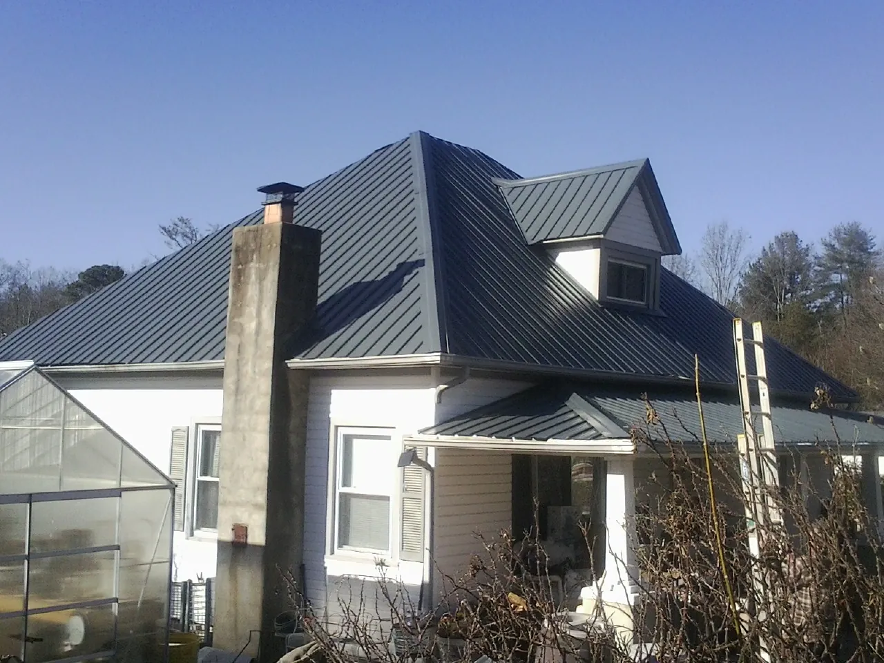 Dark blue standing seam metal roof on a white farmhouse with dormer — Slate & Tile Roof Repair by Roofing Brothers in Woodlawn