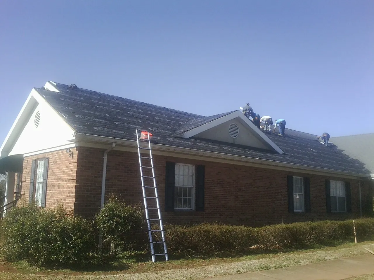 Crew tearing shingles off a brick ranch roof with a ladder set — Emergency Roof Repair work by our crew in Woodlawn