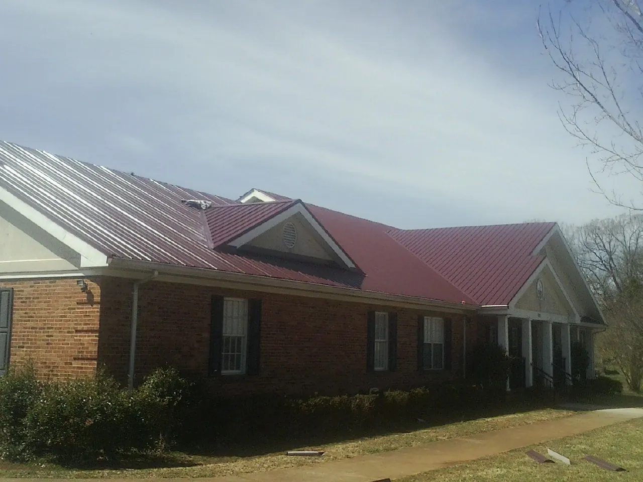 Red metal roof with gabled entries on a long brick building, from a Hail Damage Roof Repair job in Woodlawn
