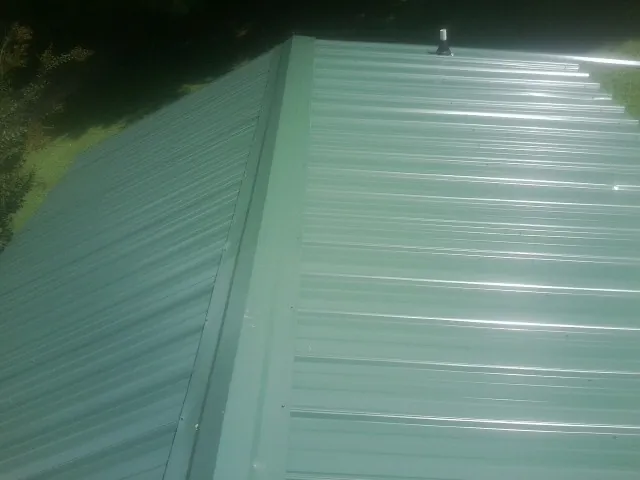 New green metal panels meeting at the ridge of a roof — Flat Roof Repair work by our crew in Woodlawn