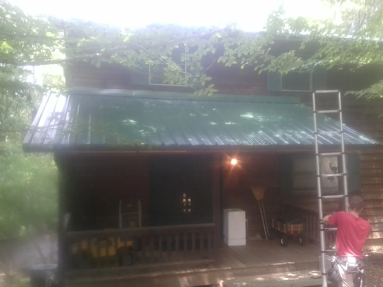 Worker on a ladder at the green porch roof of a wooded cabin in Woodlawn
