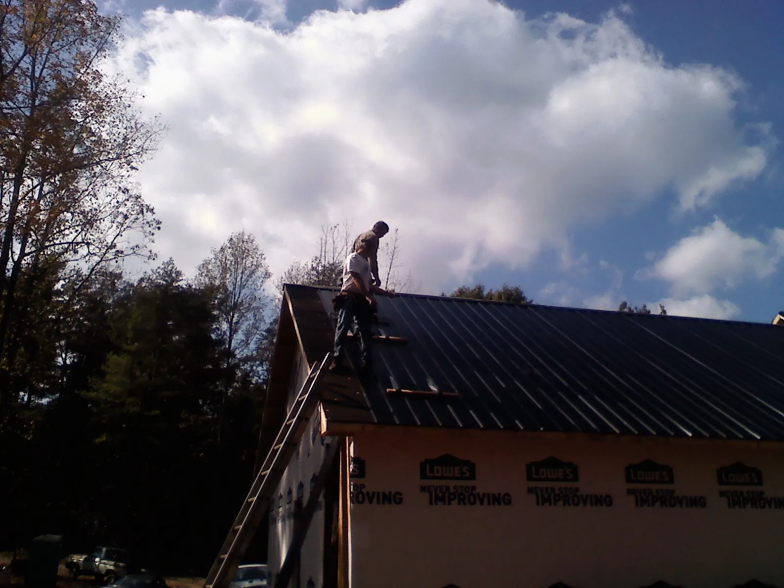 Roofer fastening dark metal panels high against a cloudy sky, from a Roof Inspection job in Woodlawn