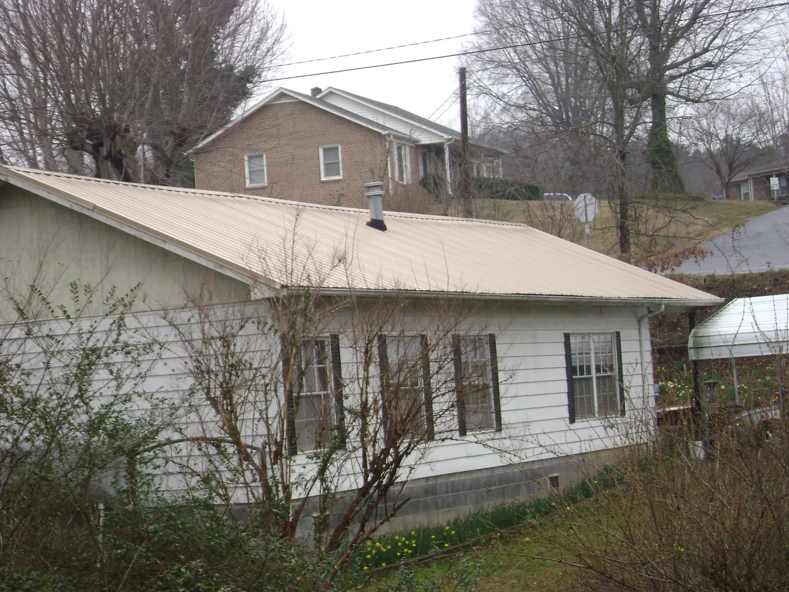 Tan metal roof on a white sided house set into a hillside — Commercial Roofing by Roofing Brothers in Woodlawn