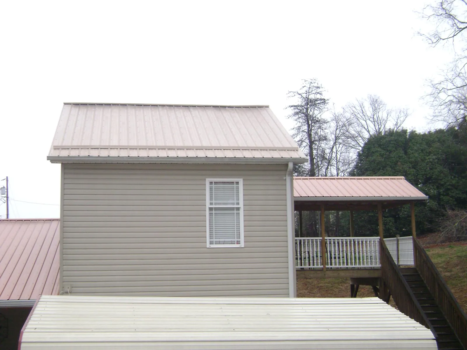 Tan metal roofs on a two story addition and attached porch, from a Roof Replacement job in Woodlawn
